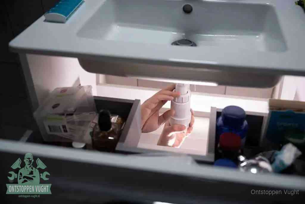 Een pompfles met zeep boven een wastafel, de heet water en afwasmiddel-methode om een vetprop in de afvoer los te maken in Vught
