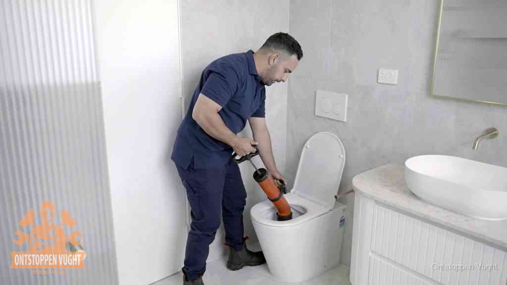 Een monteur buigt over een wandcloset en duwt met de hand een persluchtontstopper in de toiletpot om de verstopping handmatig los te maken in Vught