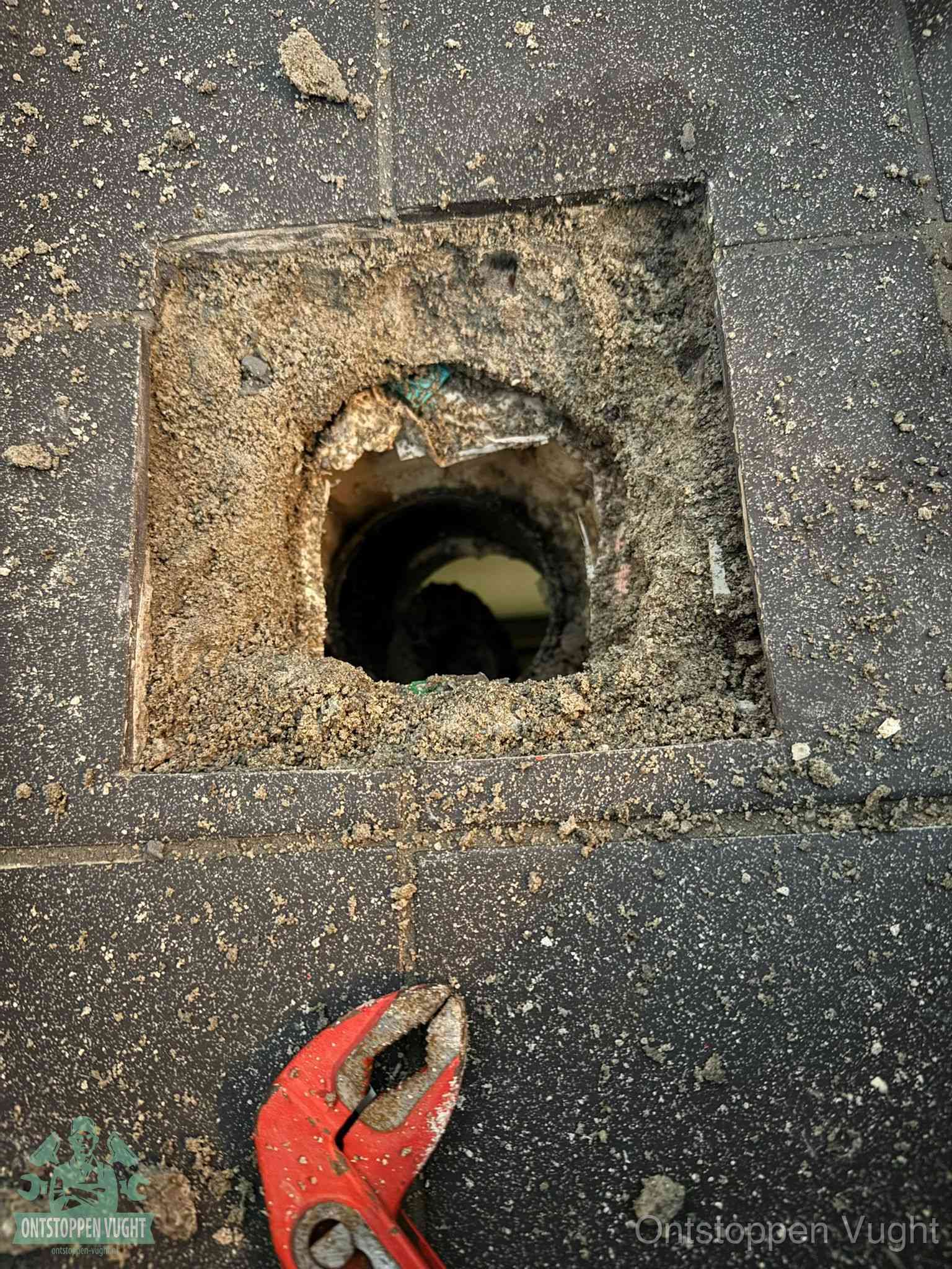 Een geopend rioolputje in een betontegelvloer met losgemaakt rooster en een zichtbare ronde afvoerbuis, het achterhalen waar de afvoerverstopping zit in Vught