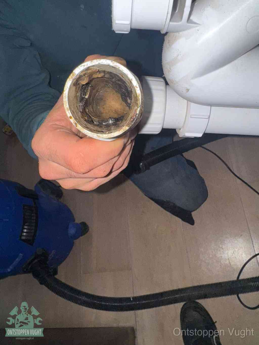Een hand houdt een losgekoppeld PVC-afvoerbuisstuk vast dat van binnen volledig is dichtgeslibd met vet, vuil en aanslag, de meest voorkomende oorzaak van een verstopte afvoer in Vught