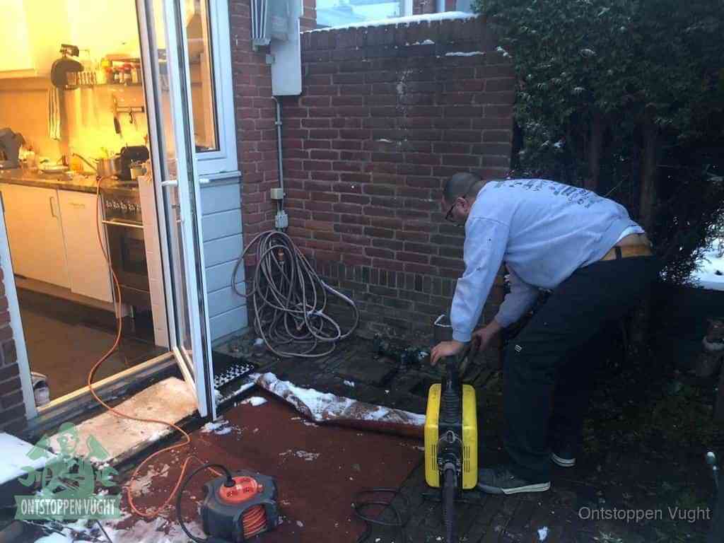 Een monteur werkt buiten bij een open riool-/grondput met een elektrische ontstoppingsmachine om een verborgen afvoerprobleem op te sporen in Vught