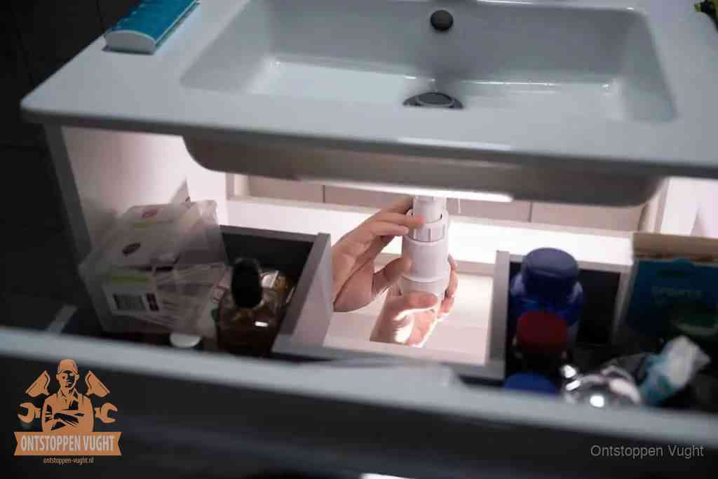 Een pompfles met zeep boven een wastafel in de toiletruimte, de warm water en afwasmiddel-methode om de wc te ontstoppen in Vught