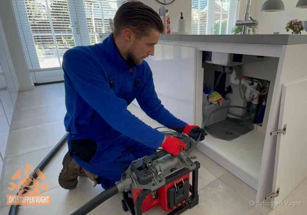 Een monteur voert een professionele elektrische ontstoppingsmachine in de afvoer onder de spoelbak tijdens het gootsteen ontstoppen in Vught